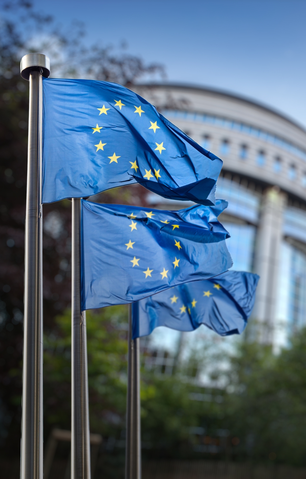 European Parliament building in Brussels with EU flags flying against a sunny background