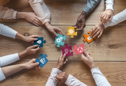 People with their hands on a table each holding a piece of a puzzle